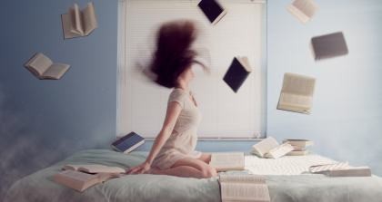 Eine Frau ist auf einem Bett von einem Sturm aus Büchern umgeben