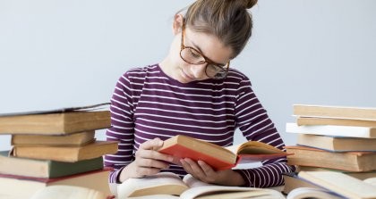 Die beste Hilfe für Autoren in der Corona-Krise ist das Hamstern von Büchern. Eine junge Leserin in einem Berg aus Büchern macht es vor.